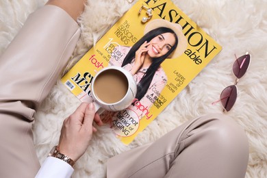 Woman with fashion magazine and cup of coffee sitting on floor, top view