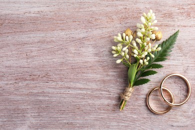 Photo of Small stylish boutonniere and rings on light wooden table, top view. Space for text