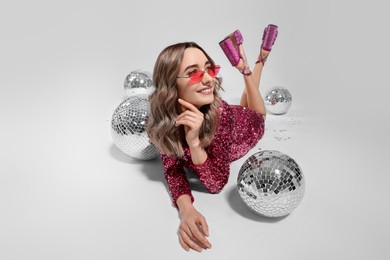 Beautiful woman in sunglasses and sequin dress among disco balls on white background