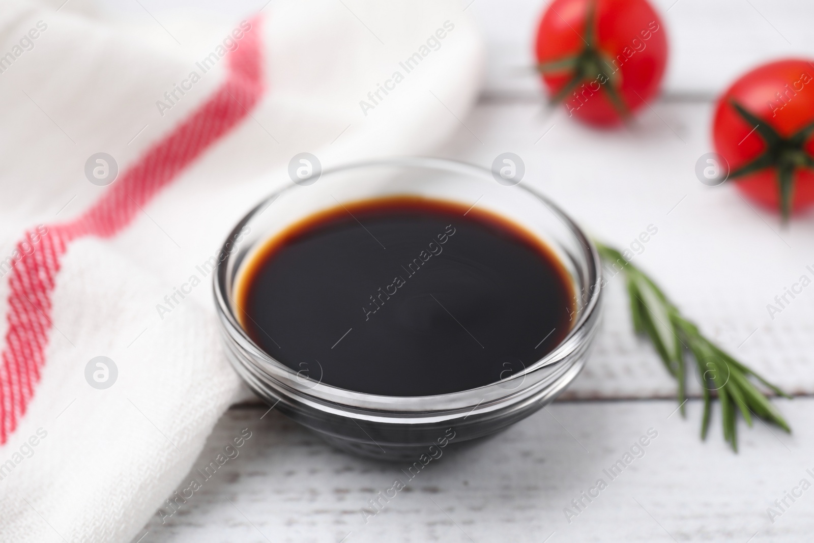 Photo of Bowl with balsamic vinegar, rosemary and tomatoes on white wooden table, closeup