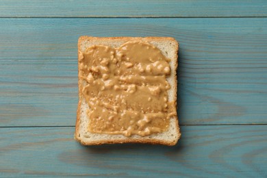 Photo of Delicious toast with peanut butter on light blue wooden table, top view