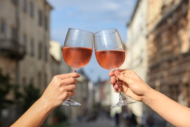 Photo of Women clinking glasses with rose wine outdoors, closeup