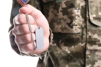 Man in camouflage uniform holding military ID tag on white background, closeup