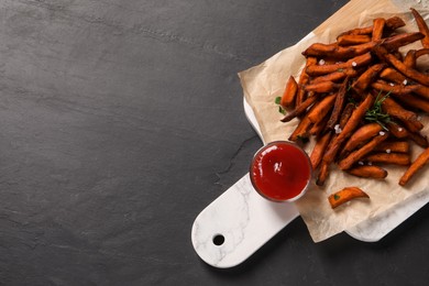 Photo of Board with delicious sweet potato fries and sauce on black table, top view. Space for text