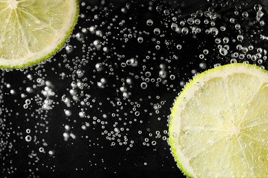 Photo of Juicy lime slices in soda water against black background, closeup