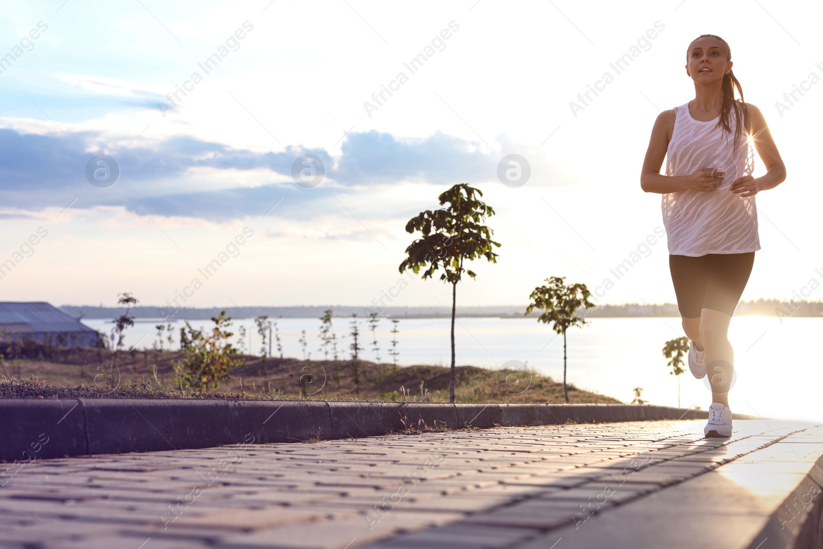 Photo of Young woman running near river in morning. Space for text