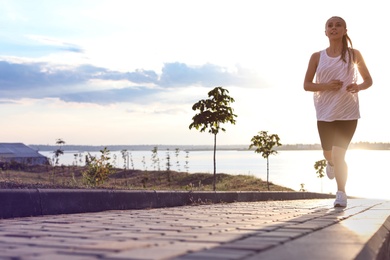 Photo of Young woman running near river in morning. Space for text