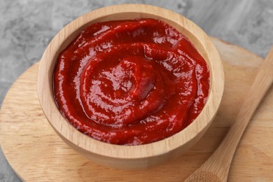 Photo of Organic ketchup in wooden bowl and spoon on grey table, closeup. Tomato sauce