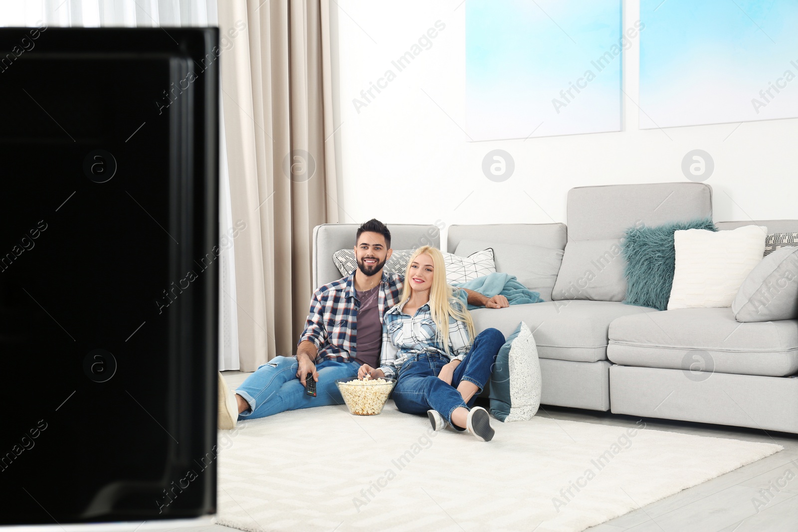 Photo of Young couple with bowl of popcorn watching TV on floor at home