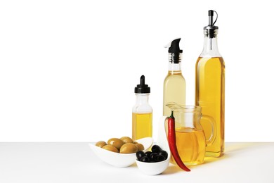 Photo of Bottles of different cooking oils, olives and chili pepper on white background, space for text