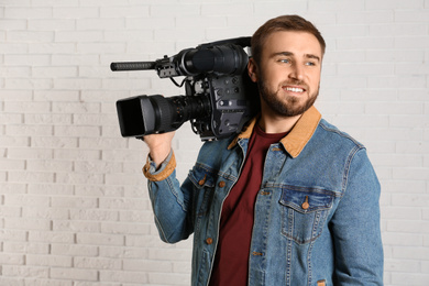 Photo of Operator with professional video camera near white brick wall