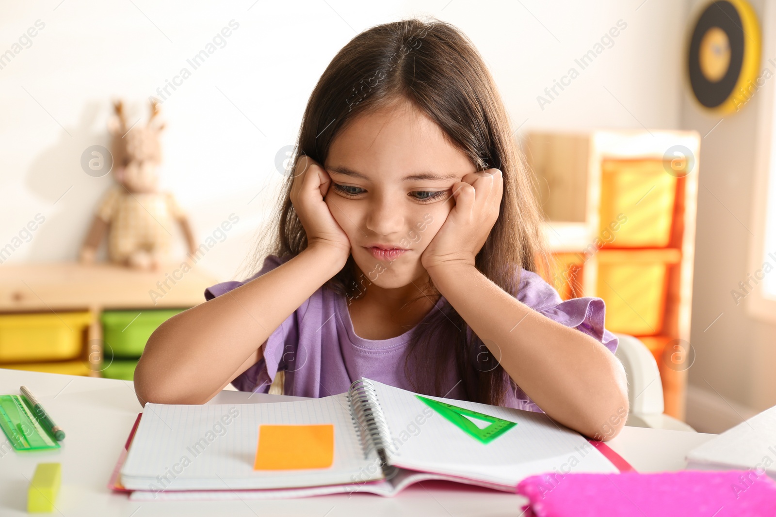 Photo of Emotional little girl doing homework at table indoors