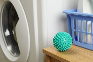 Photo of Turquoise dryer ball on wooden table near washing machine