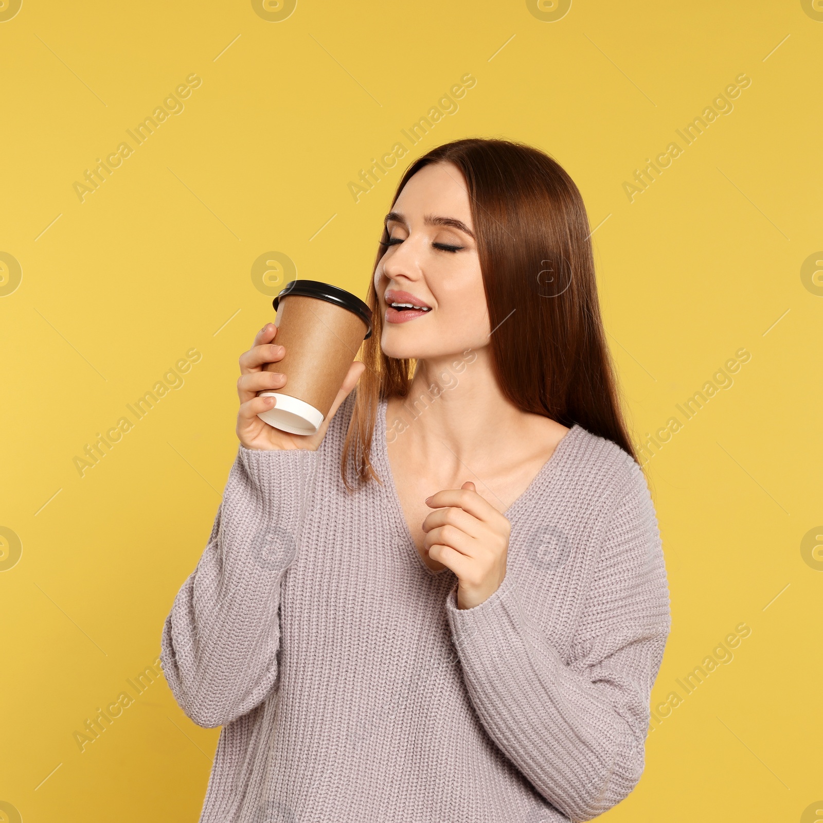 Photo of Beautiful young woman in sweater with drink on yellow background. Winter season