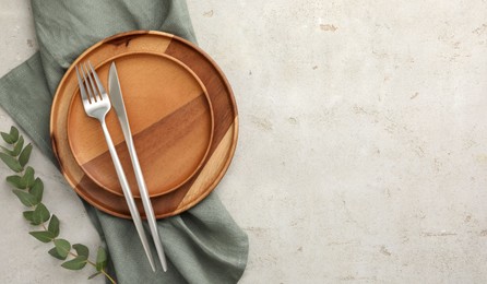 Stylish setting with cutlery, napkin, eucalyptus branch and plates on light table, top view. Space for text