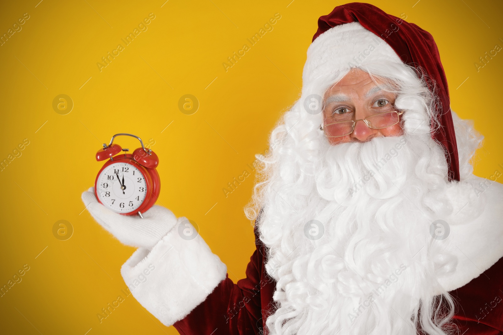 Photo of Santa Claus holding alarm clock on yellow background. Christmas countdown