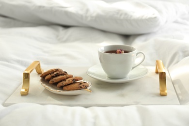 Cup of aromatic tea and cookies on soft blanket in bedroom