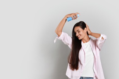 Photo of Woman applying dry shampoo onto her hair on light grey background. Space for text