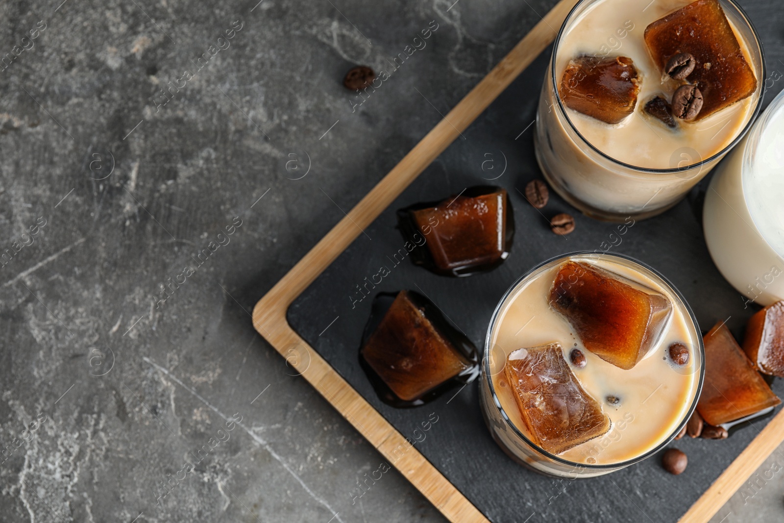 Photo of Glasses of milk with coffee ice cubes on grey table, top view. Space for text