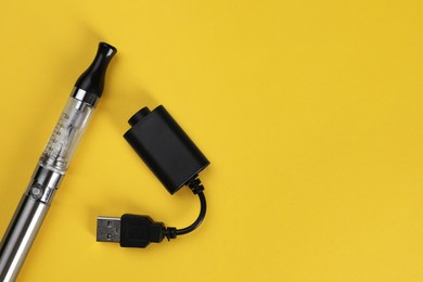 Photo of Reusable electronic cigarette and USB charger on yellow background, flat lay. Space for text
