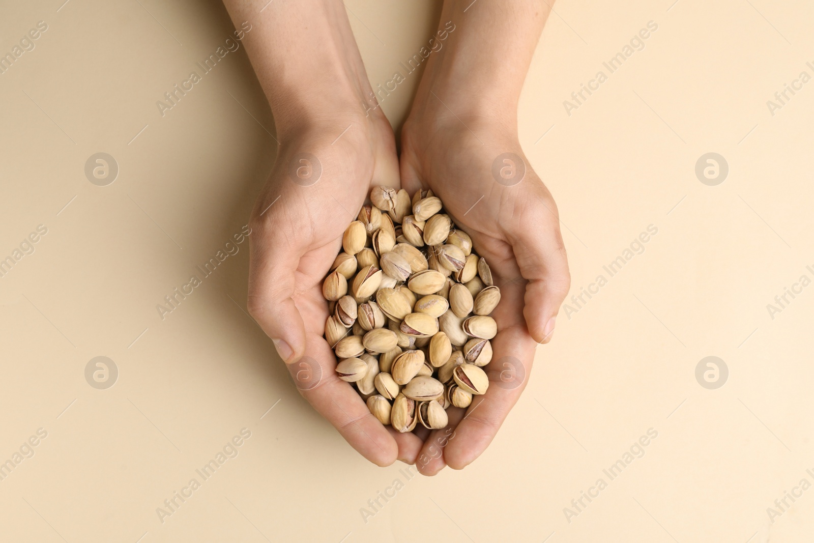 Photo of Woman holding tasty roasted pistachio nuts on beige background, top view