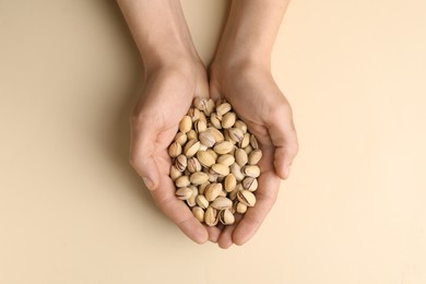 Woman holding tasty roasted pistachio nuts on beige background, top view