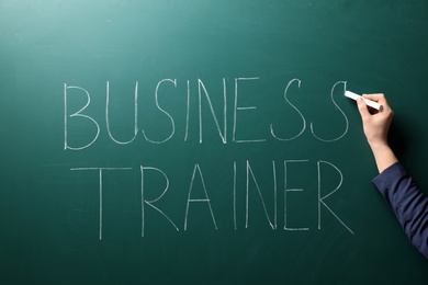 Woman writing text BUSINESS TRAINER on chalkboard. Coaching concept