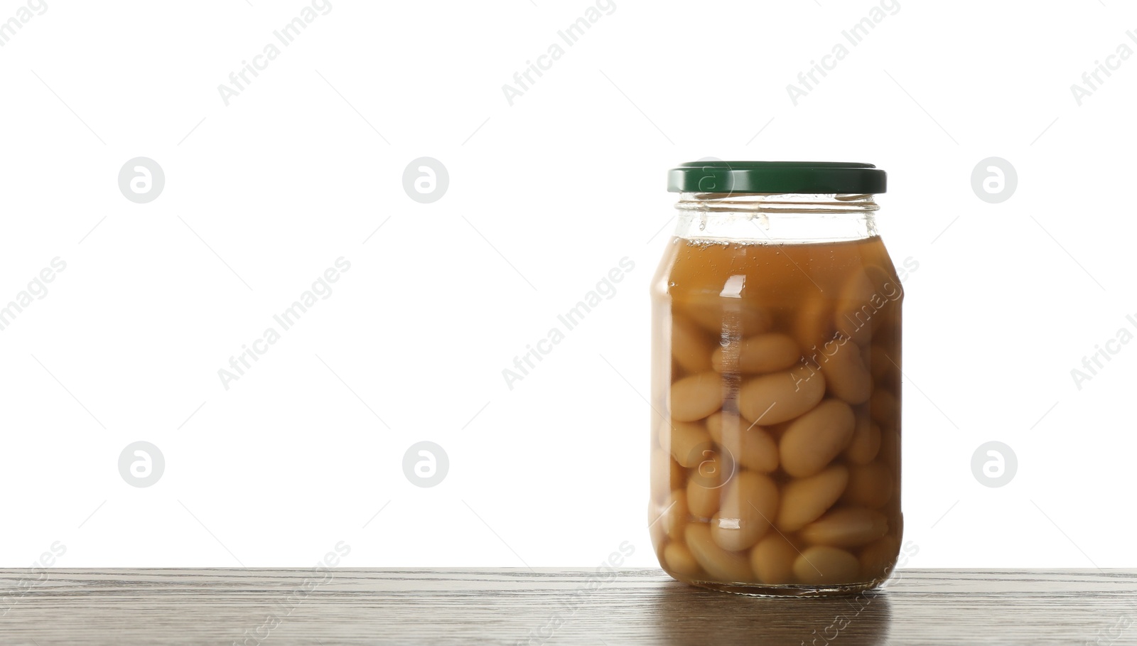 Photo of Glass jar of pickled beans on wooden table against white background. Space for text