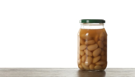 Photo of Glass jar of pickled beans on wooden table against white background. Space for text