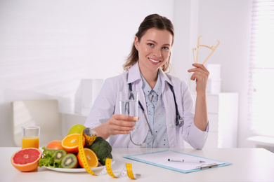 Photo of Nutritionist with glass of water and caliper at desk in office