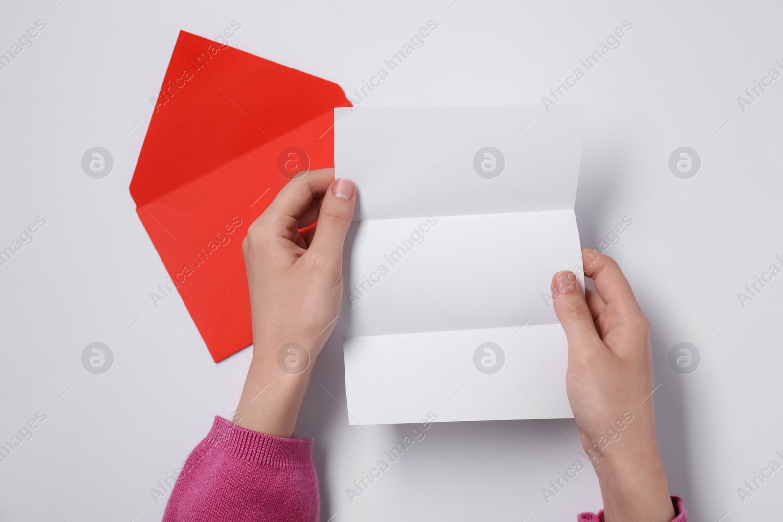 Photo of Woman with blank sheet of paper and letter envelope at white table, top view. Space for text