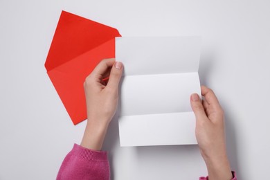 Photo of Woman with blank sheet of paper and letter envelope at white table, top view. Space for text