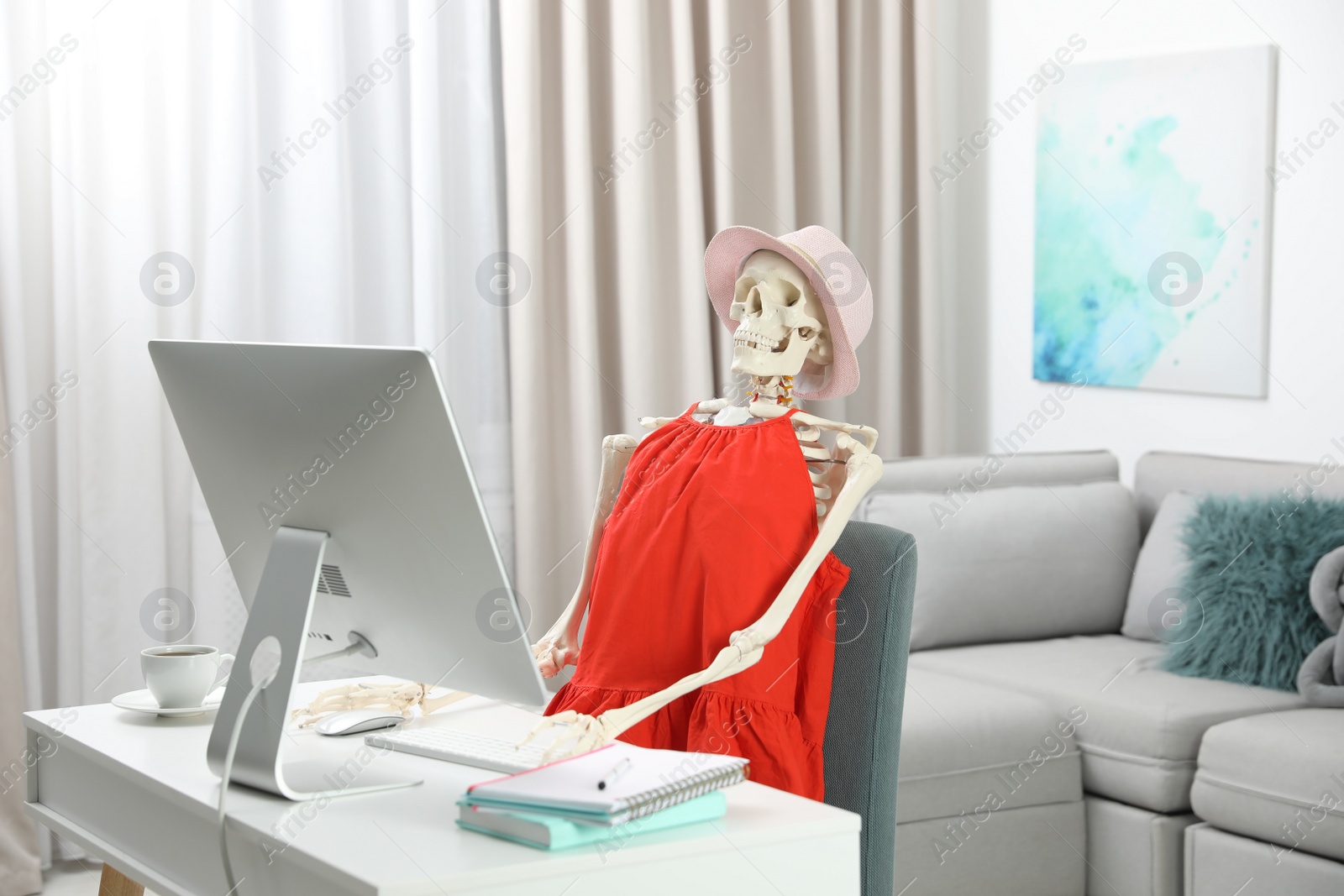 Photo of Human skeleton in red dress using computer indoors