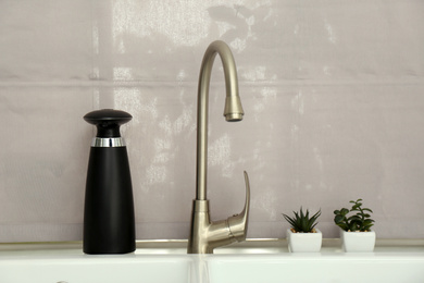 Photo of Modern automatic soap dispenser near sink indoors