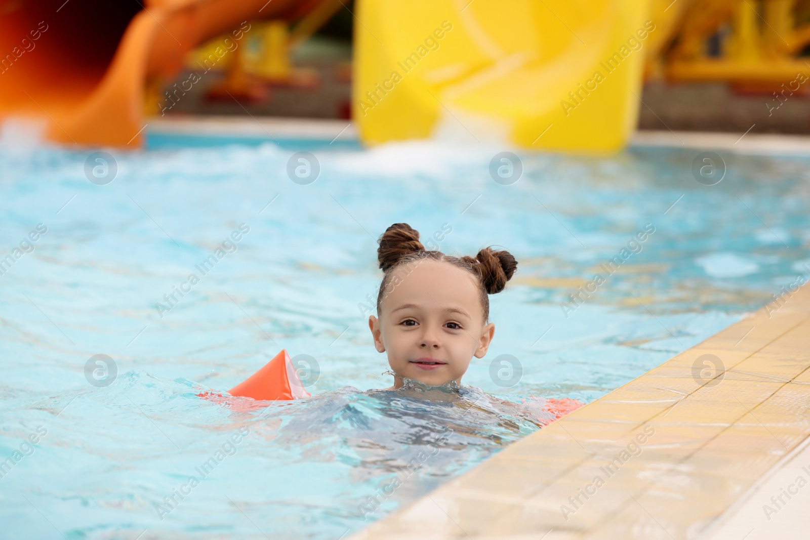Photo of Cute little girl with inflatable sleeves in swimming pool at water park