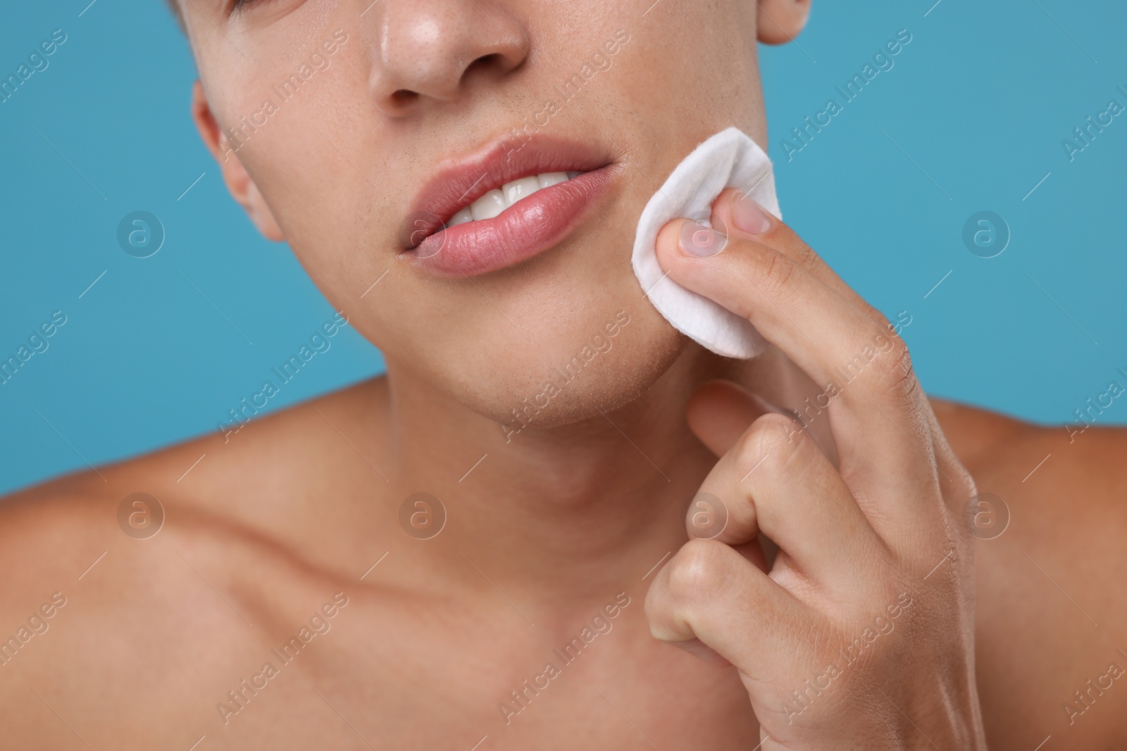 Photo of Man cleaning face with cotton pad on light blue background, closeup