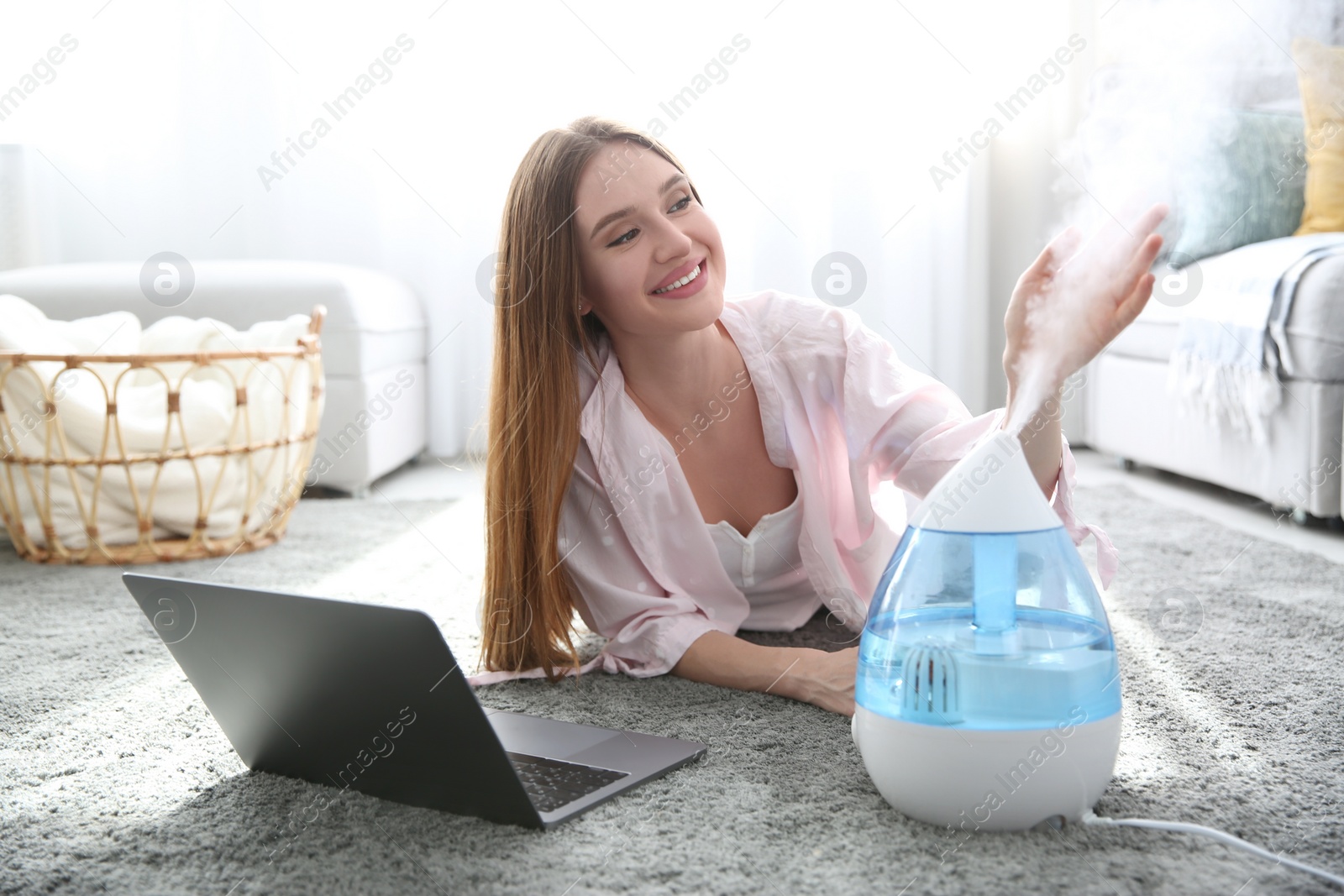 Photo of Woman with laptop near modern air humidifier at home
