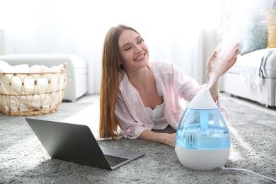 Woman with laptop near modern air humidifier at home