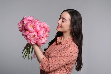 Photo of Beautiful young woman with bouquet of peonies on light grey background