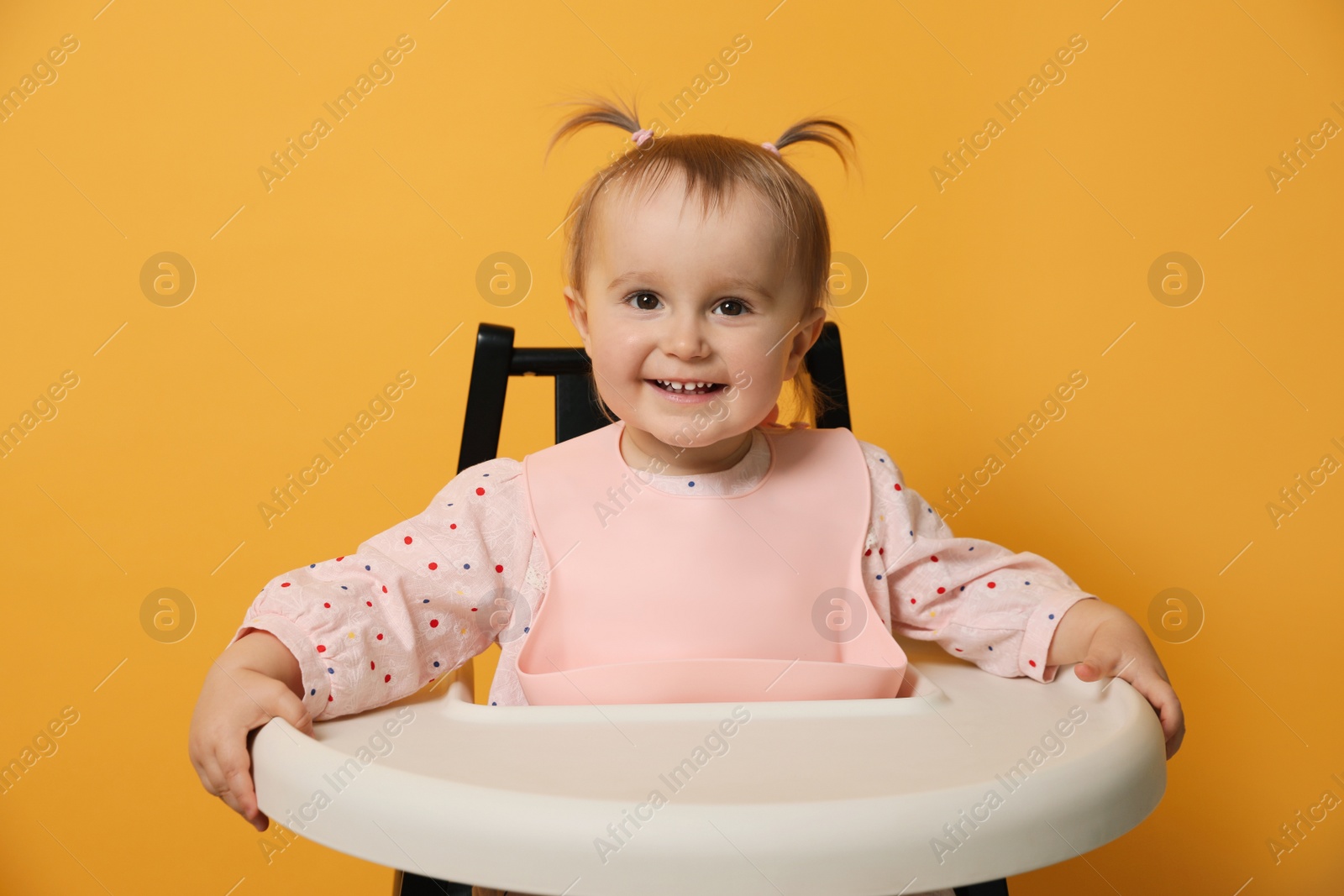 Photo of Cute little baby wearing bib in highchair on yellow background