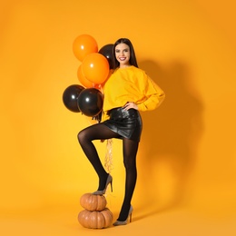 Photo of Beautiful woman with balloons and pumpkins on yellow background. Halloween party