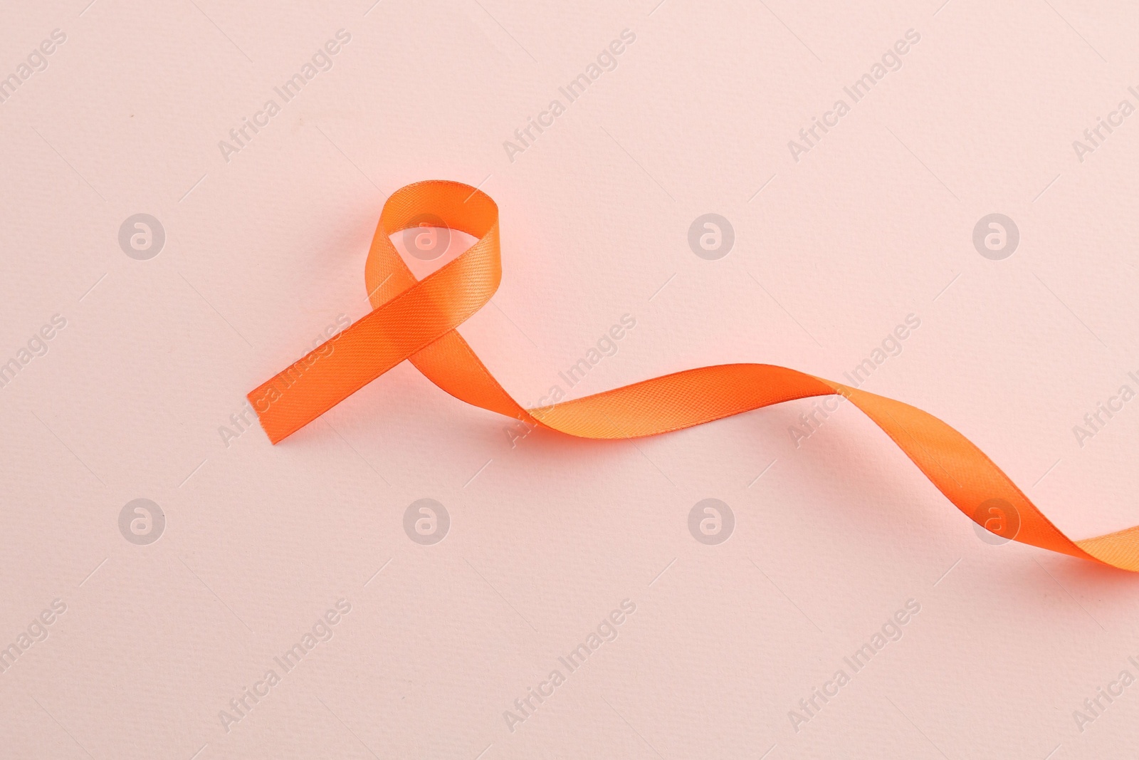 Photo of Orange awareness ribbon on beige background, top view