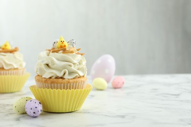 Tasty Easter cupcake with vanilla cream and candies on white marble table, space for text