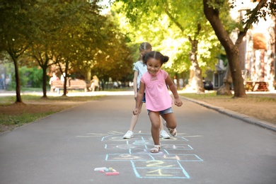 Photo of Little children playing hopscotch drawn with colorful chalk on asphalt