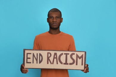 Photo of African American man holding sign with phrase End Racism on light blue background