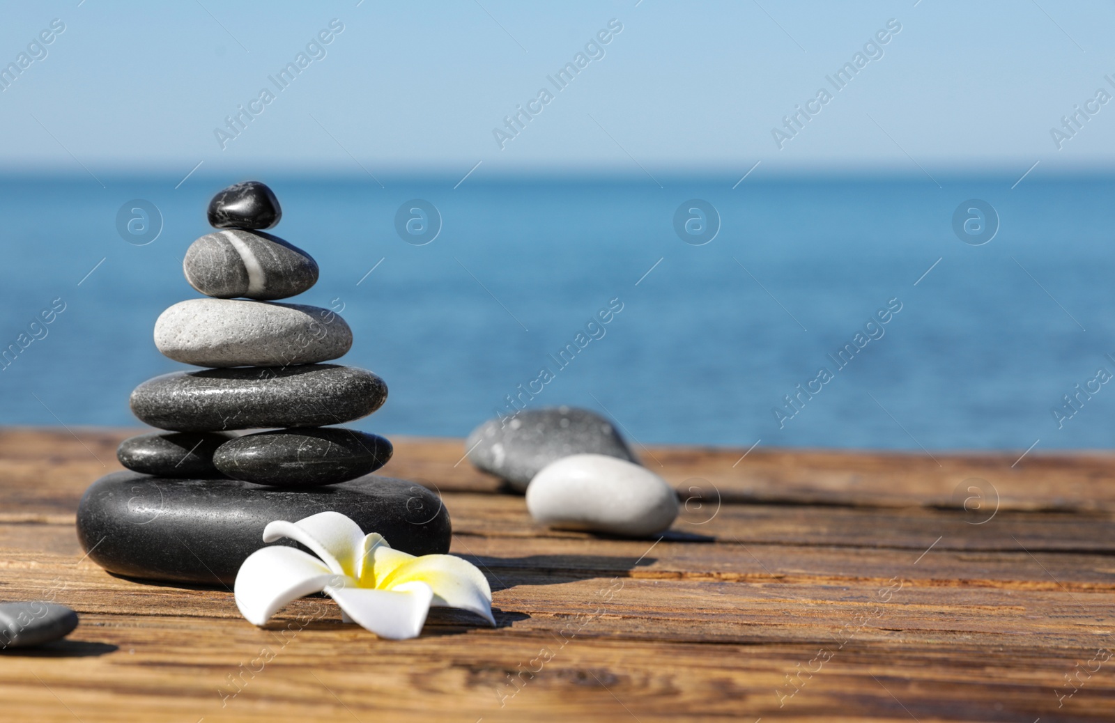 Photo of Stack of stones and flower on wooden pier near sea, space for text. Zen concept