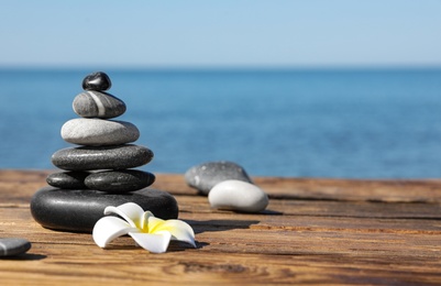 Photo of Stack of stones and flower on wooden pier near sea, space for text. Zen concept