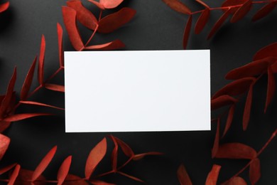 Photo of Blank business card and red eucalyptus branches on black background, flat lay. Mockup for design