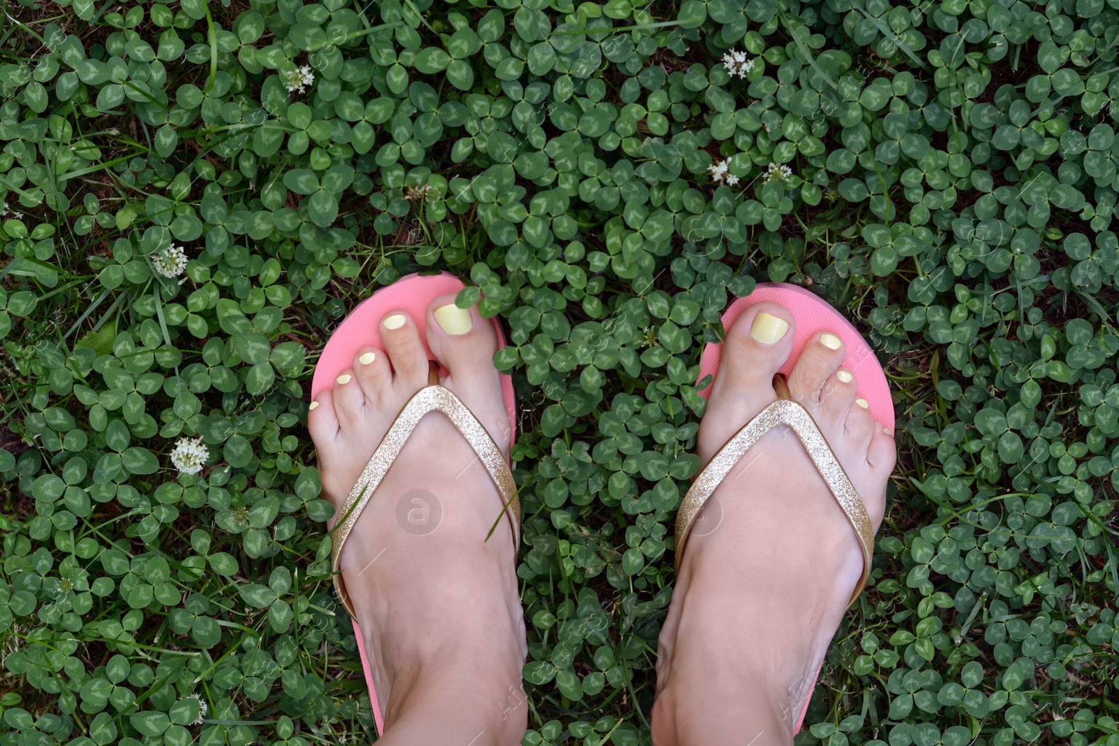 Photo of Woman wearing stylish flip flops on green grass outdoors, top view