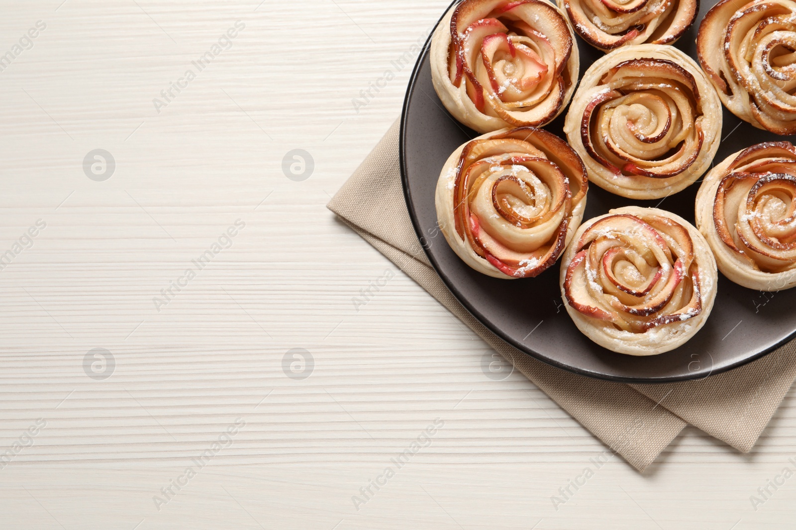 Photo of Freshly baked apple roses on white wooden table, top view. Space for text